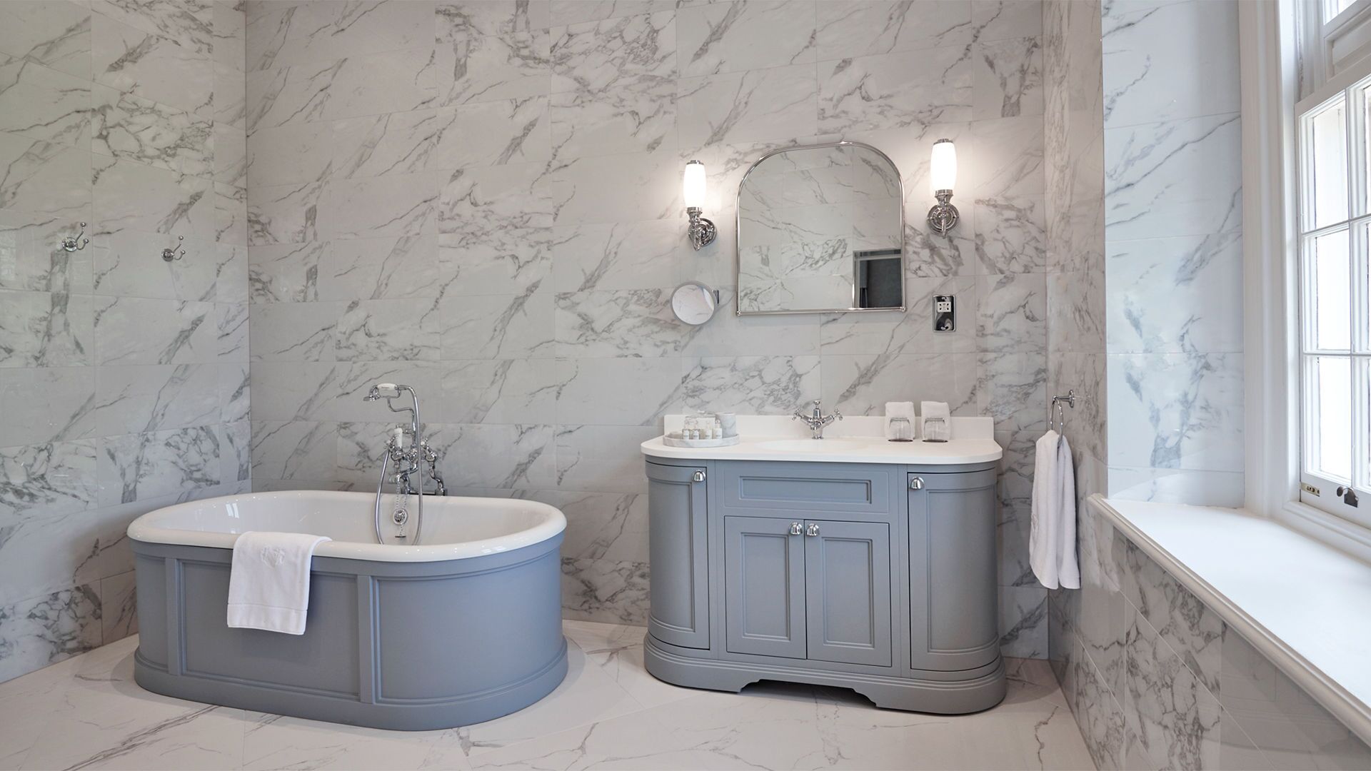 A bathroom with a freestanding bathtub, a vanity with a mirror, and marble walls.