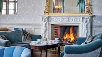 A room with a fireplace, sofas, a table with teacups, and a patterned wall.