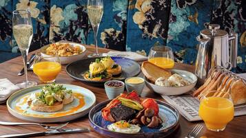 Un desayuno con diversas opciones de comida, bebidas y un sofá estampado con motivos florales al fondo.