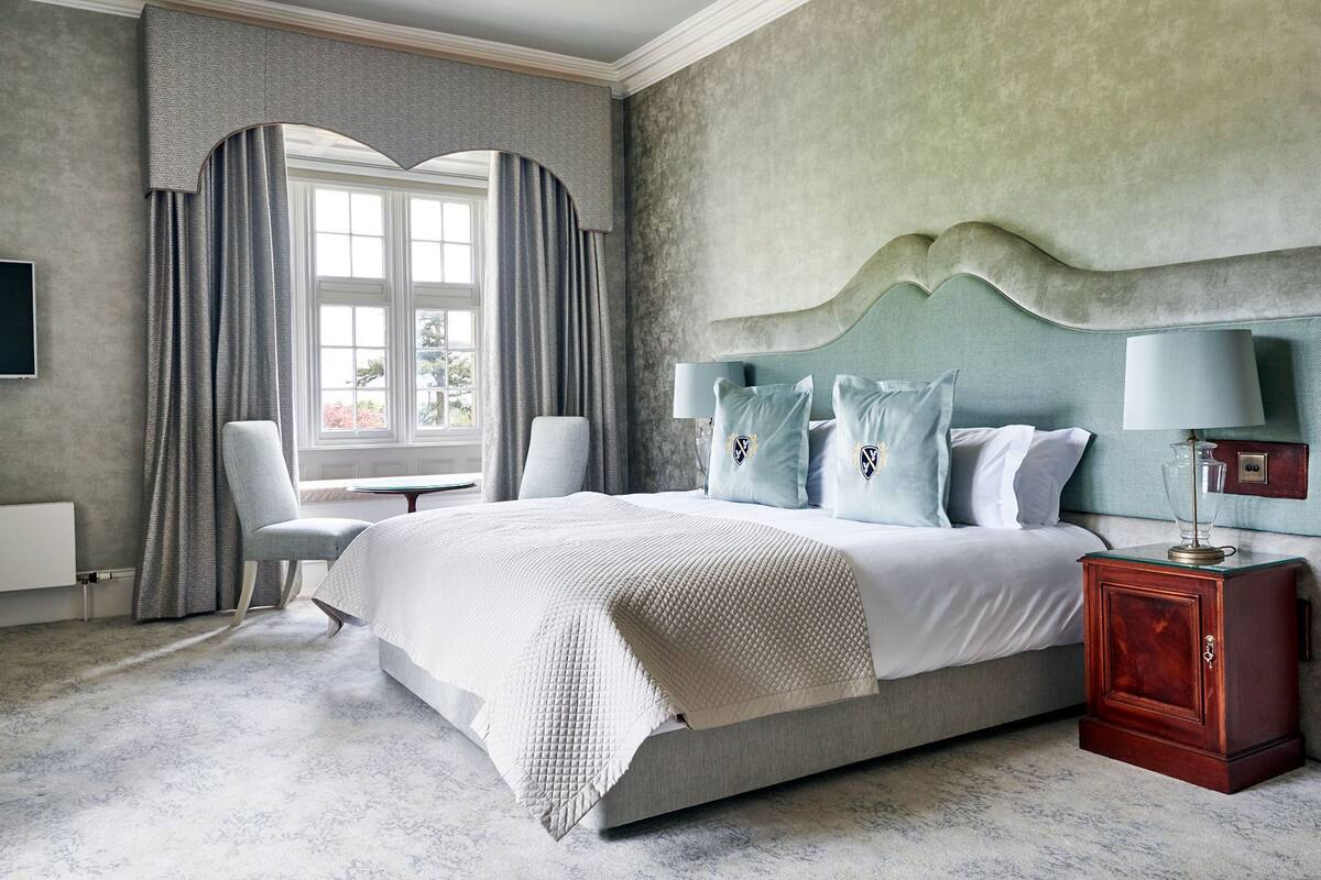 A bedroom with a large bed, a nightstand, a chair, and a window with curtains.
