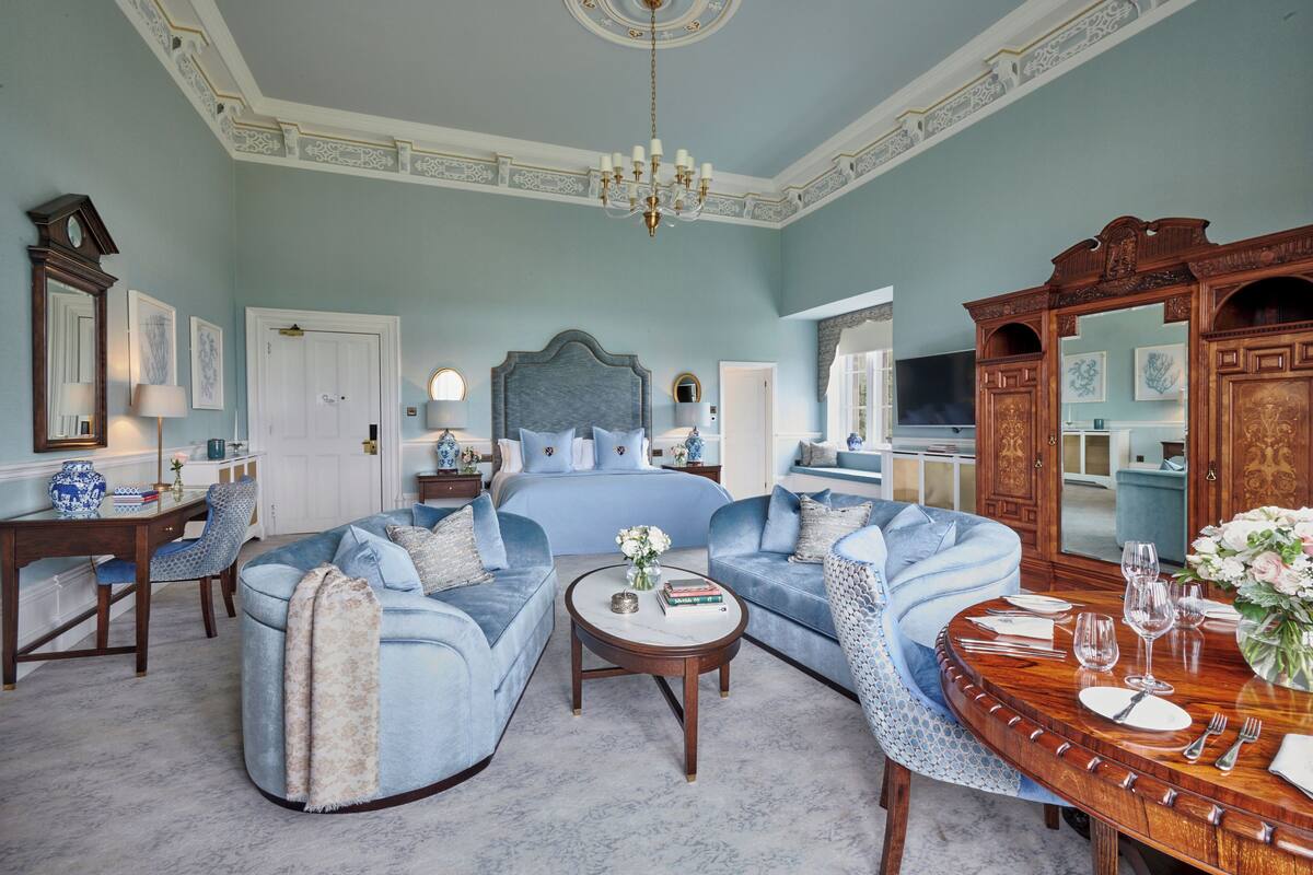 A spacious room with a large bed, a round dining table set for a meal, and a cozy seating area with a sofa and armchairs.