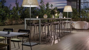 An outdoor dining area with tables and chairs, a bar counter, and two floor lamps. - AC Hotel Diagonal L'Illa by Marriott (Barcelona)