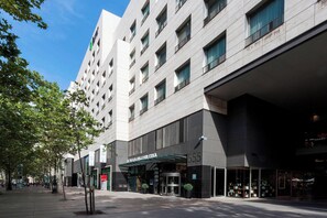 A modern hotel with a prominent entrance, large windows, and a covered area with potted plants.