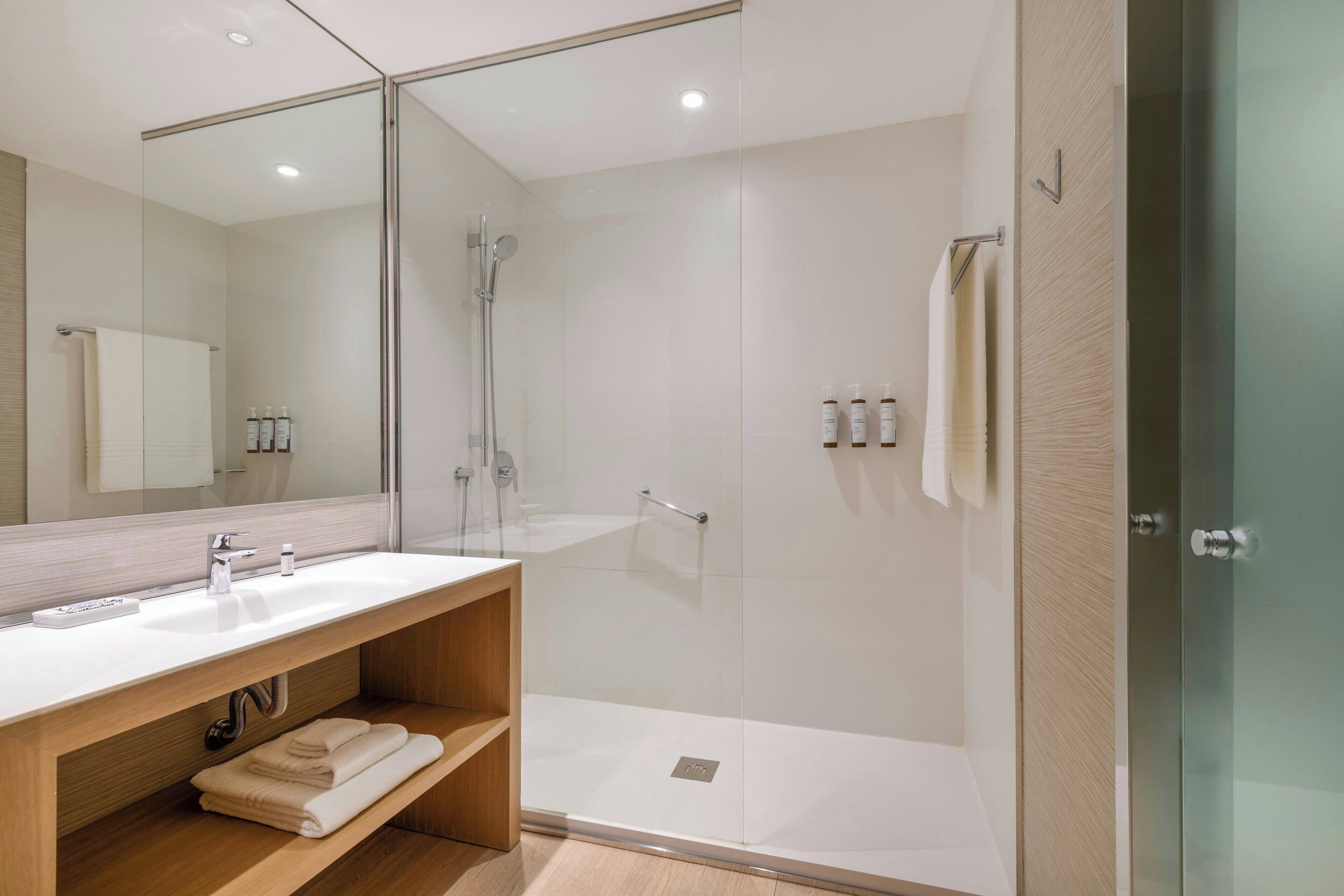 Un bagno moderno con cabina doccia in vetro, mobile bagno in legno con lavabo e uno specchio grande.