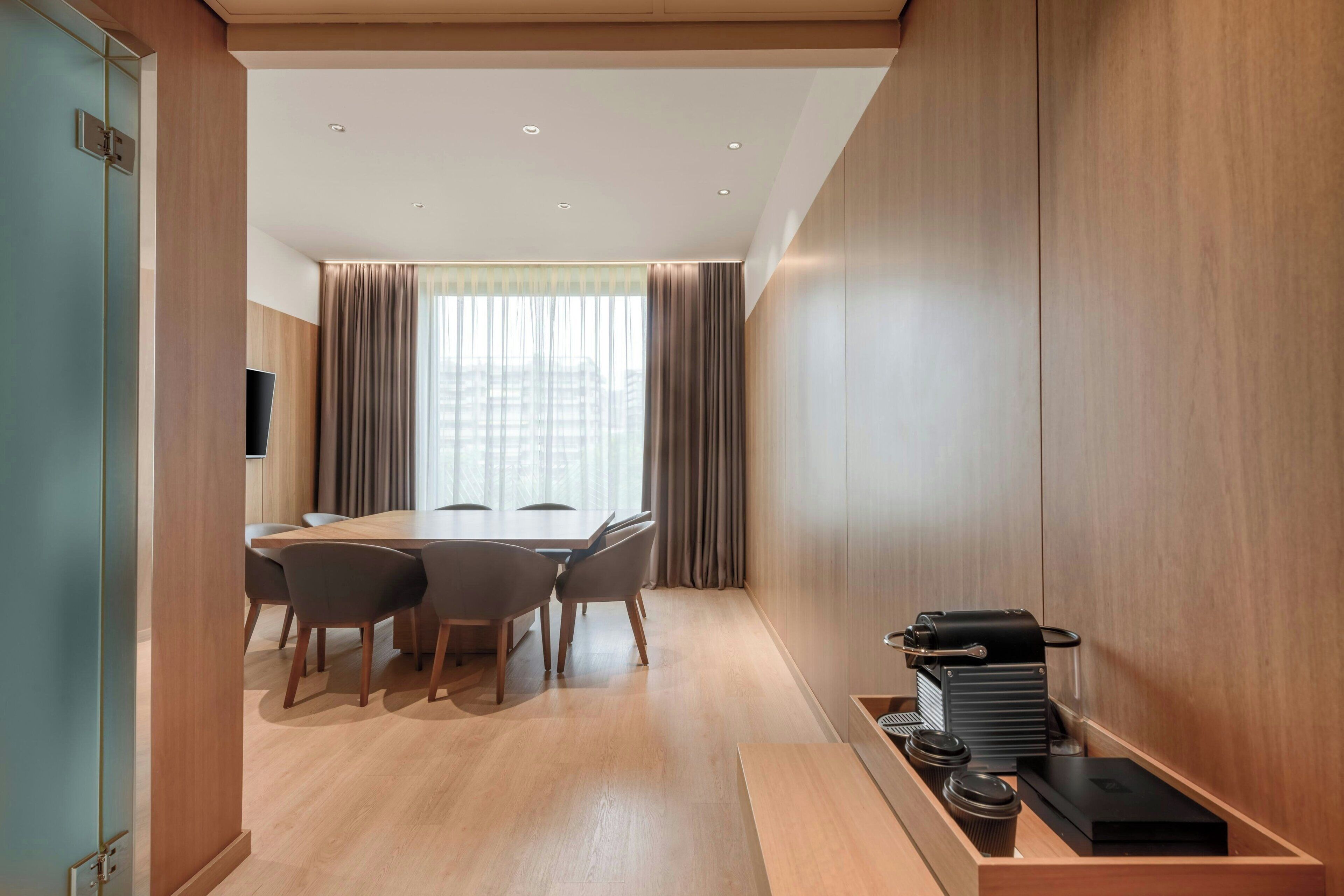 Una habitación de hotel moderna con suelo de madera, una mesa de comedor con sillas, un televisor y una cafetera.