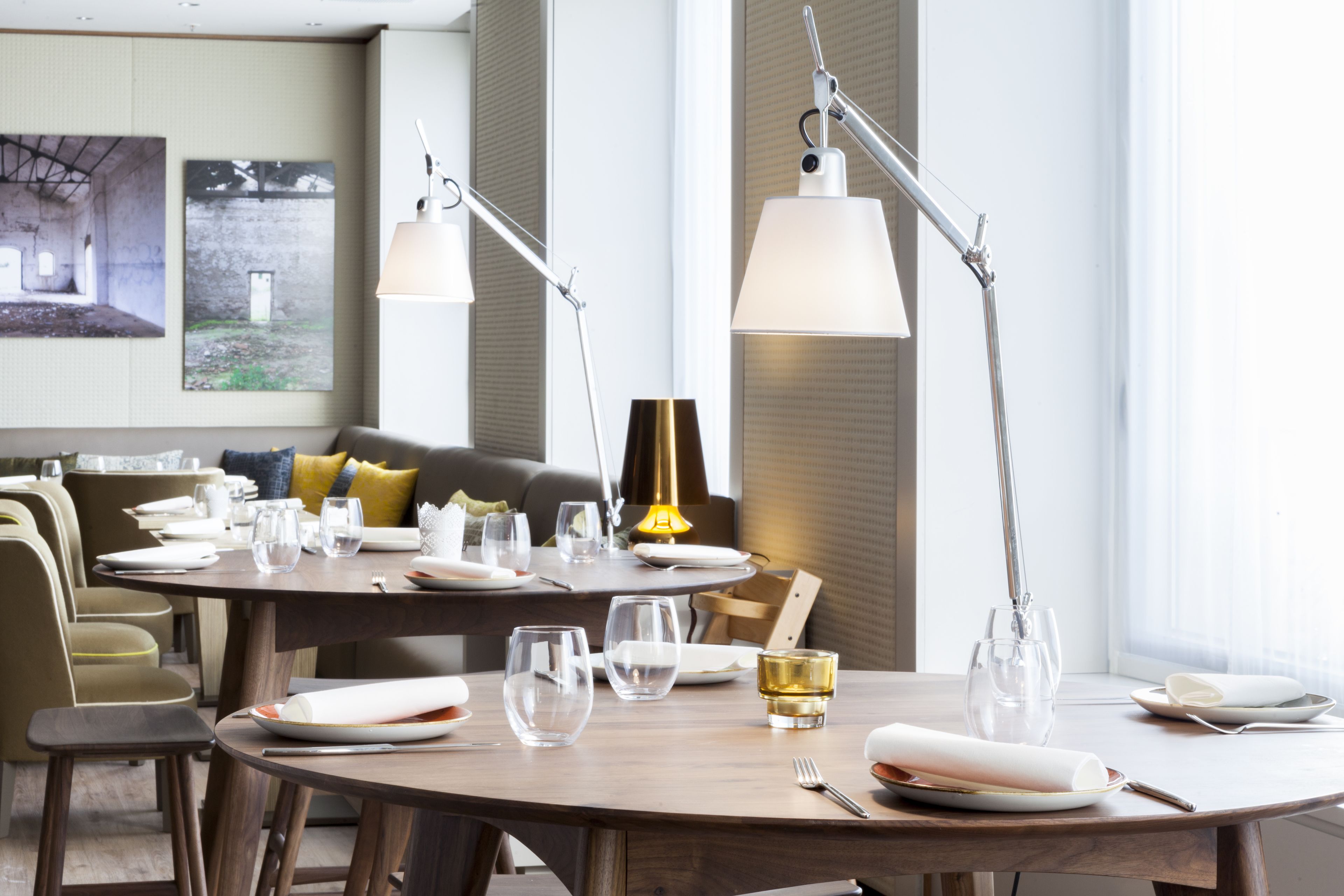 A dining area with round tables, chairs, and a sofa in the background.