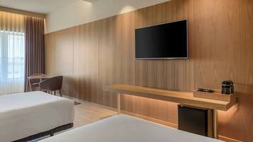 Habitación de hotel con dos camas, un televisor montado en la pared, una mesita con cafetera y una silla.