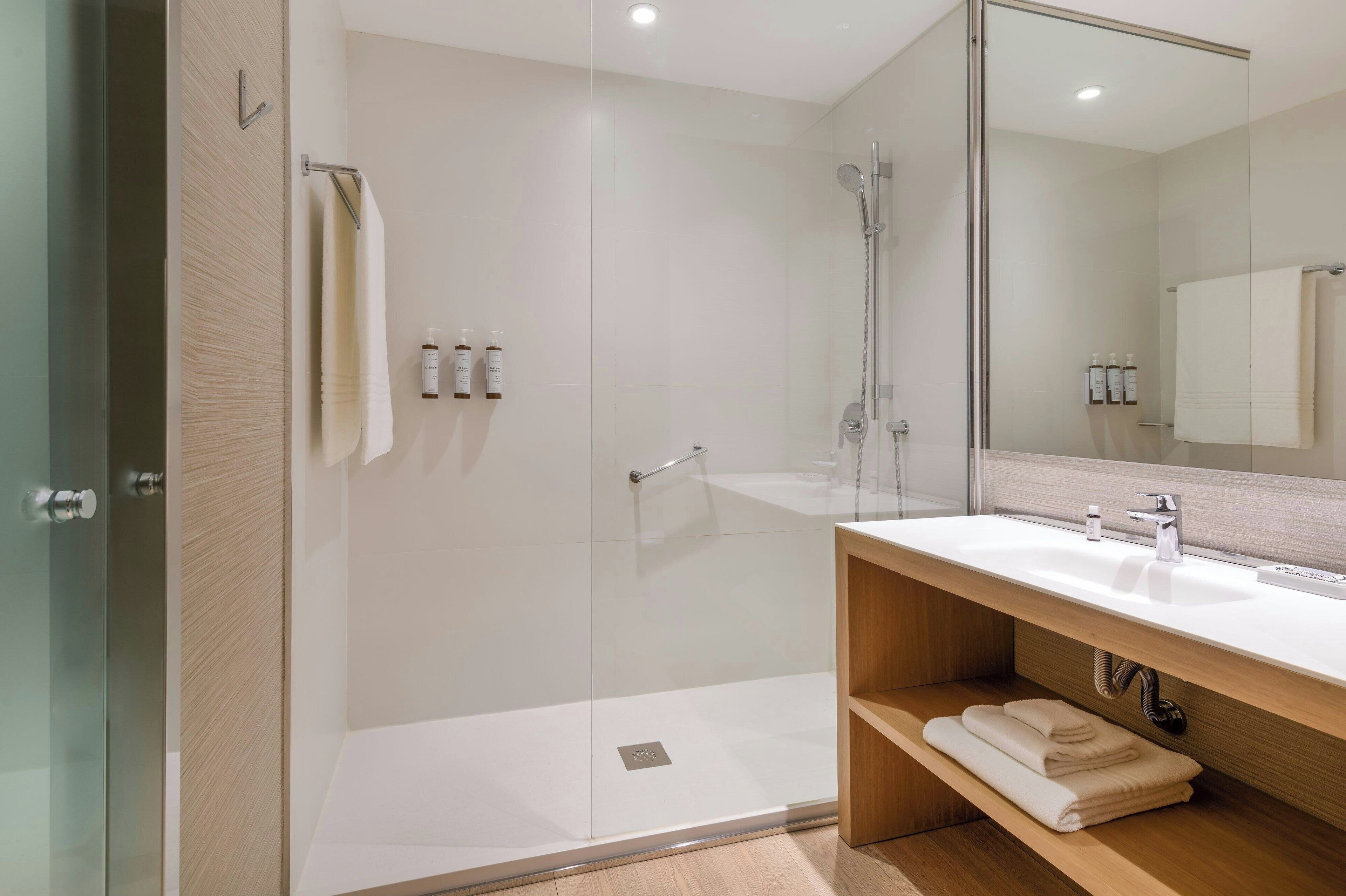 A modern bathroom with a glass-enclosed shower, a wooden vanity with a sink, and a large mirror.