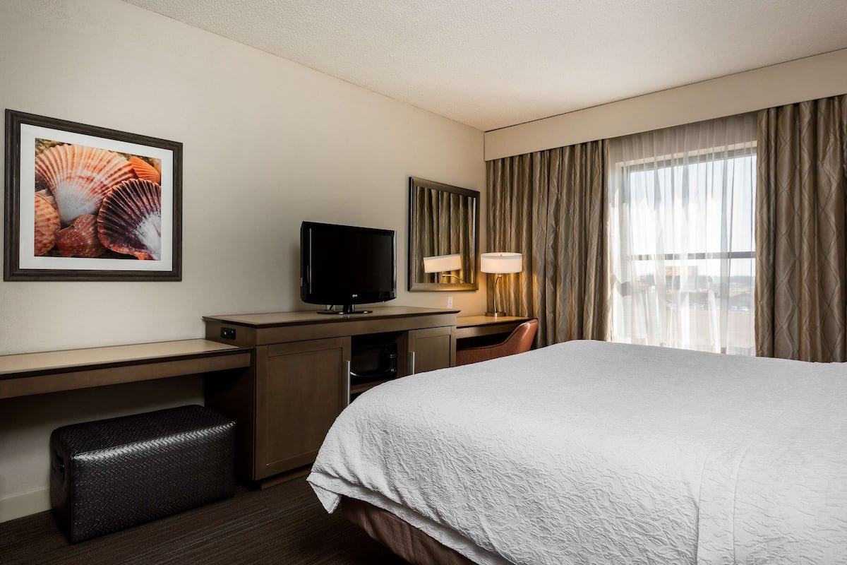 A hotel room with a bed, a desk with a television, a lamp, and a framed picture on the wall.