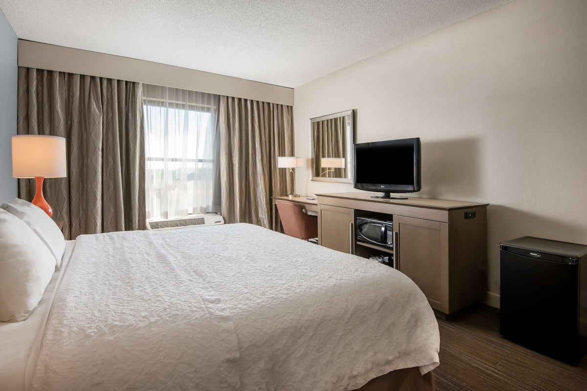 A hotel room with a bed, a desk, a television, and a refrigerator.