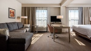 Ein Hotelzimmer mit einer Couch, einem Schreibtisch, einem Bett und einem Fernseher.