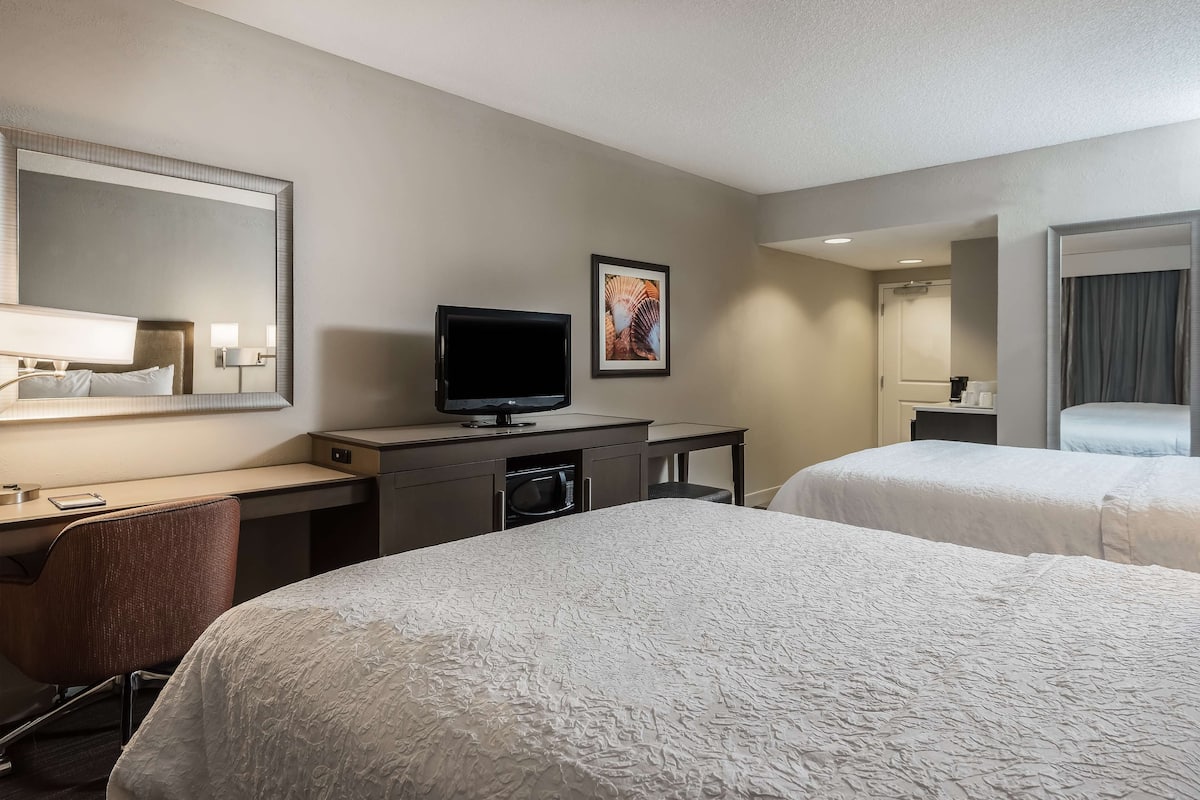 A hotel room with two beds, a desk with a computer, a TV, and a large mirror.