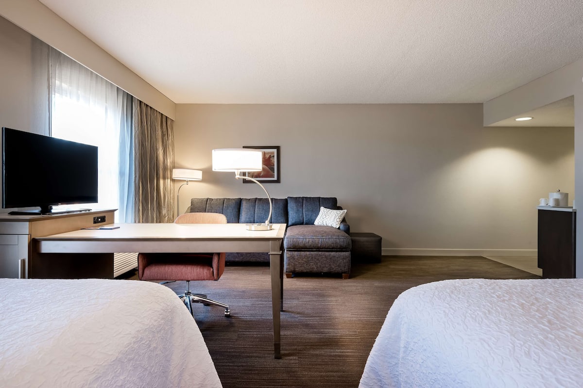 A hotel room with two beds, a desk with a TV, a sofa, and a lamp.