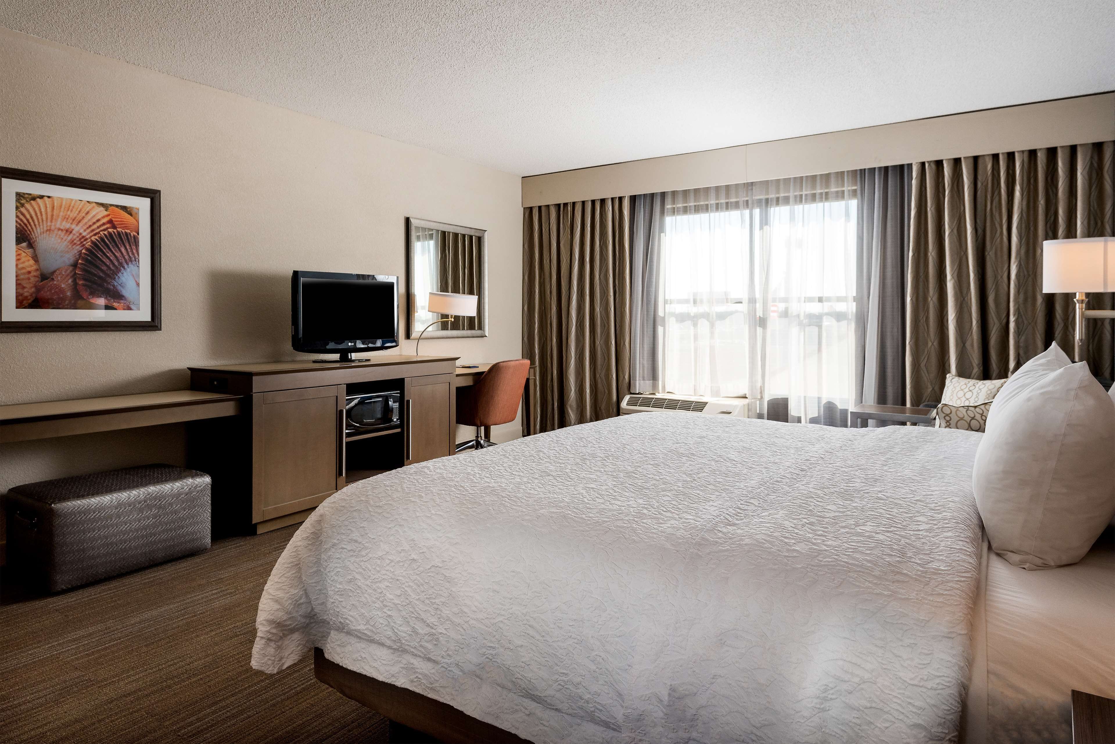 A hotel room with a large bed, a desk with a television, a chair, and a window with curtains.