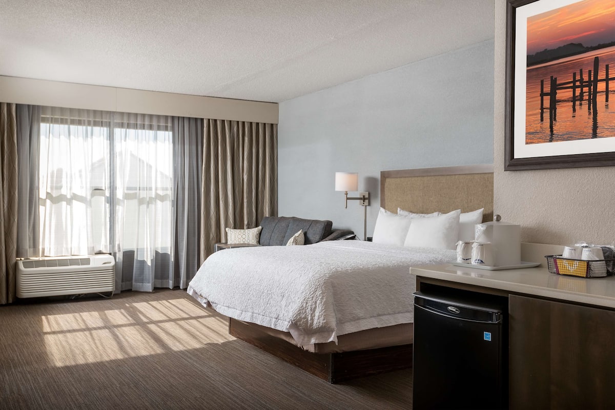 A hotel room with a bed, bedside table, lamp, and a framed picture on the wall.