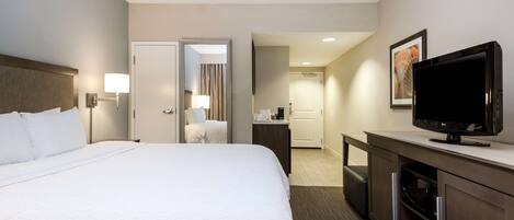 A hotel room with a large bed, a desk with a television, a mirror, and a door leading to a bathroom.
