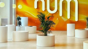 Un interior moderno con un letrero grande 'NUM', muebles blancos cilíndricos y plantas en macetas.