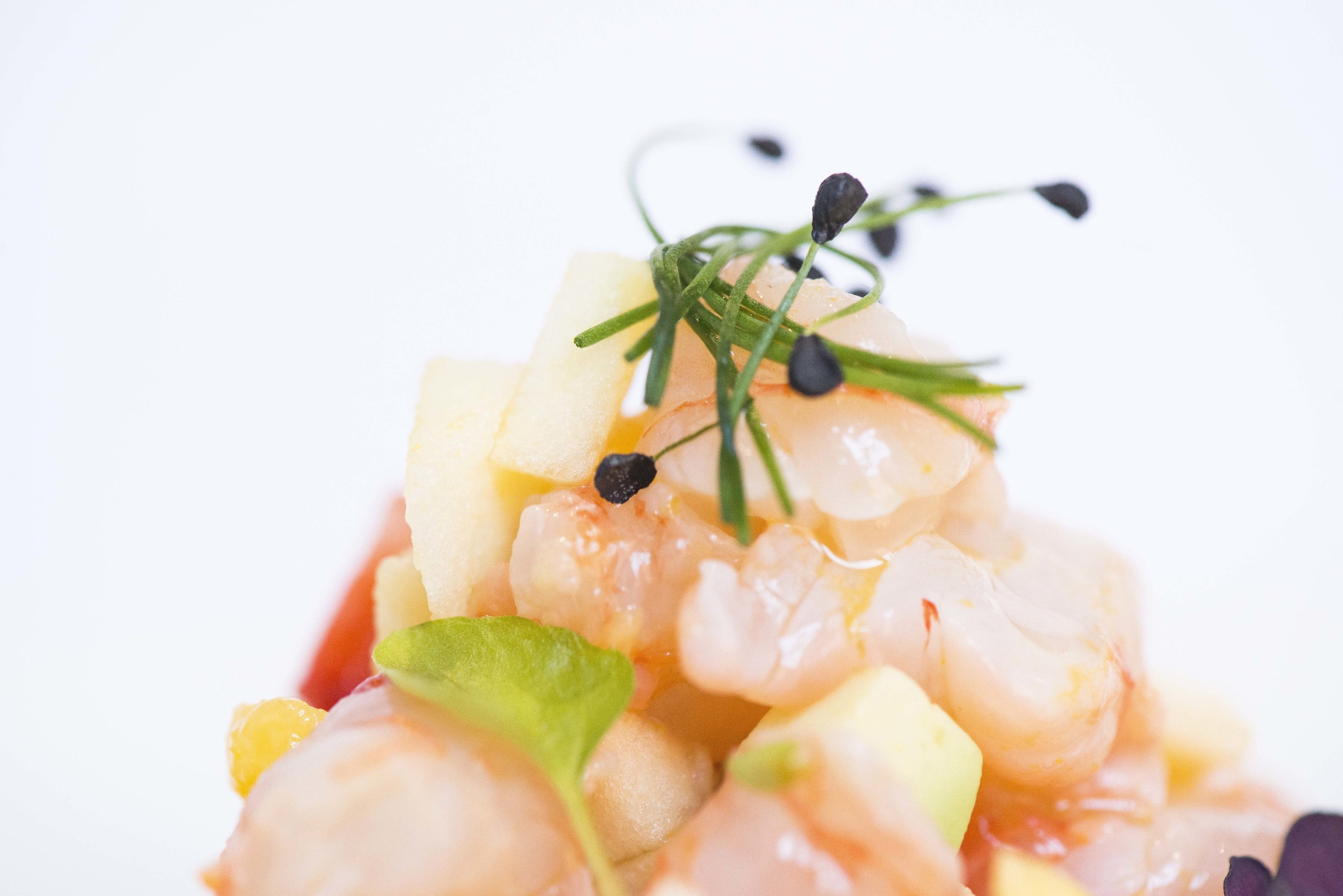 Primer plano de un plato de mariscos con camarones, verduras picadas y guarniciones.