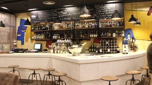 Un bar con una barra blanca, varios taburetes y estantes llenos de botellas.