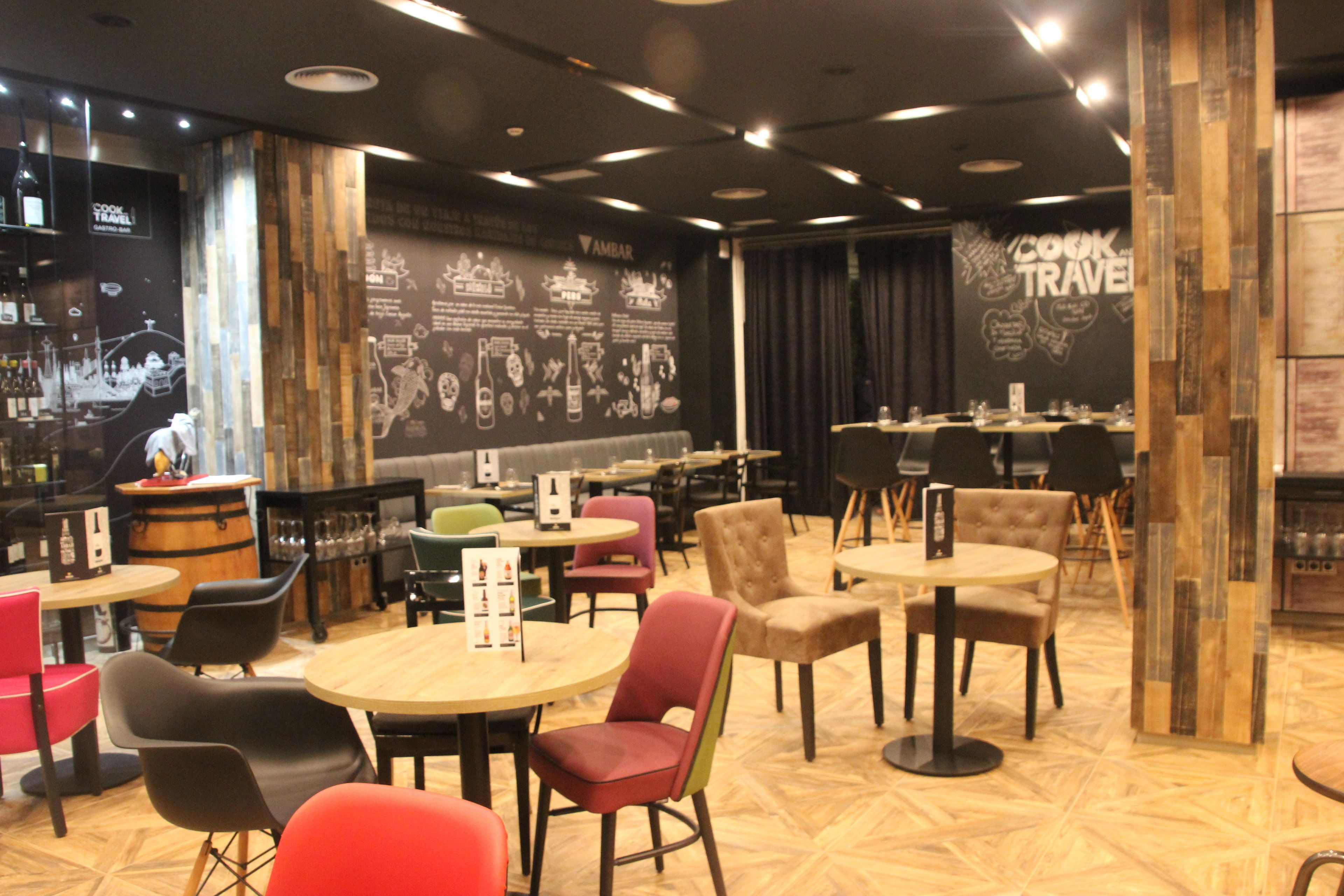 Un restaurante con mesas y sillas redondas, una zona de bar y una pared con texto y gráficos.