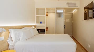 Una habitación de hotel con una cama grande, un armario, un espejo y una mesita con una lámpara.