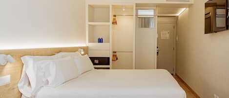 A hotel room with a large bed, a wardrobe, a mirror, and a small table with a lamp.