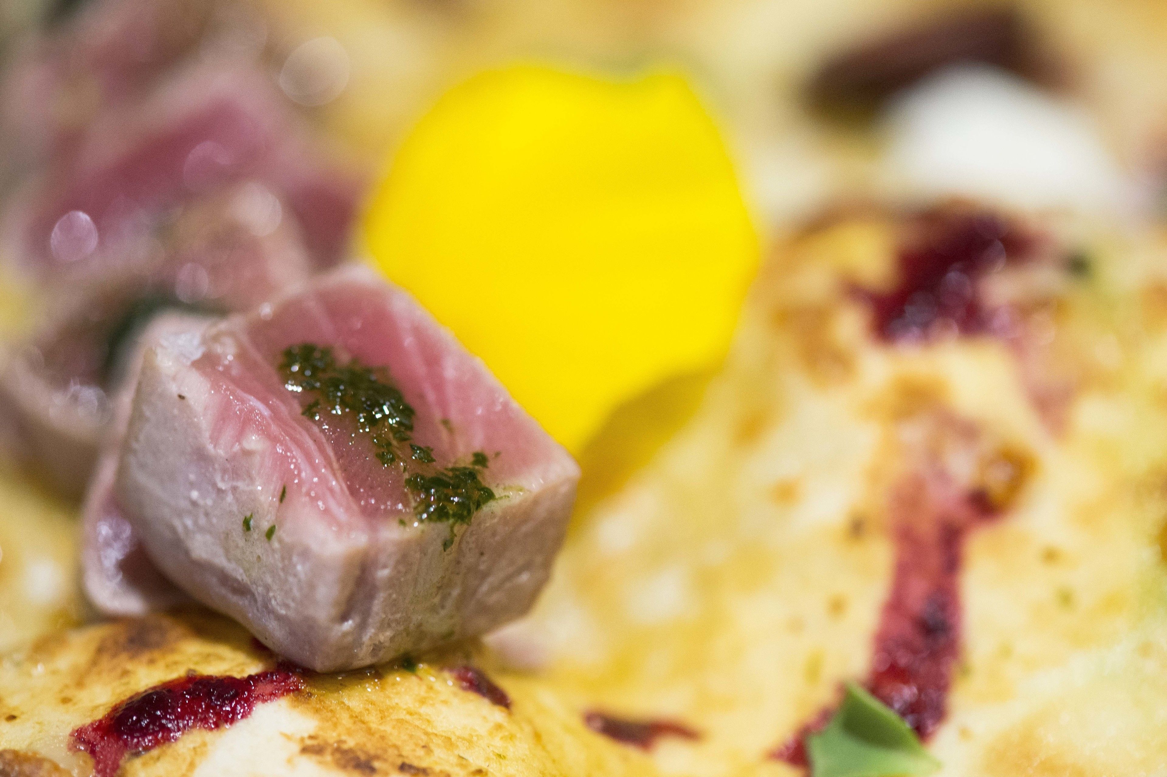 A close-up of a dish with a piece of meat, a yellow item, and some green garnish.