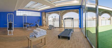 A modern gym with exercise equipment, a bench, and a table with towels and water bottles.
