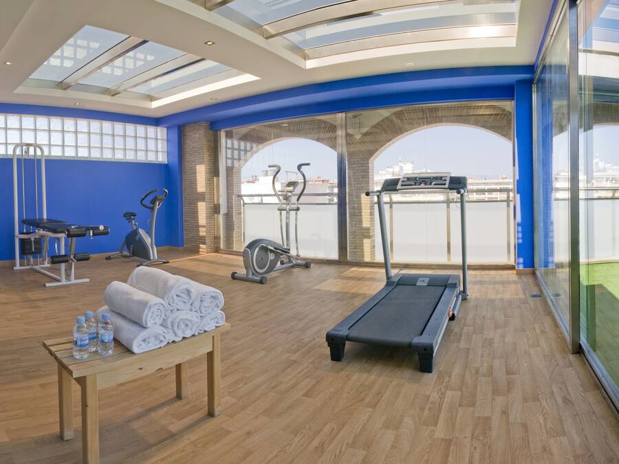 Un gimnasio moderno con equipamiento de ejercicio, una banca y una mesa con toallas y botellas de agua.
