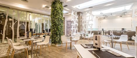 A modern restaurant with wooden flooring, white chairs, and a central green plant.