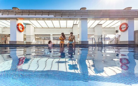 A swimming pool with clear water, surrounded by a covered area with columns and lifebuoys.