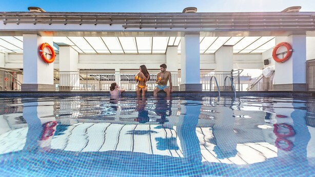 Una piscina con agua cristalina, rodeada por una zona cubierta con columnas y boyas salvavidas.