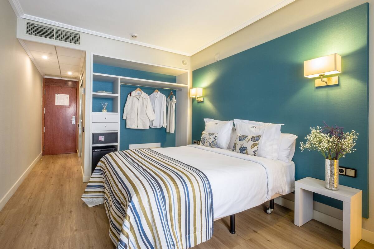 A hotel room with a bed, a wardrobe, a bedside table, and a nightstand.