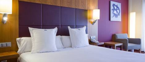 A hotel room with a large bed, two bedside tables, a chair, and a wall-mounted artwork.