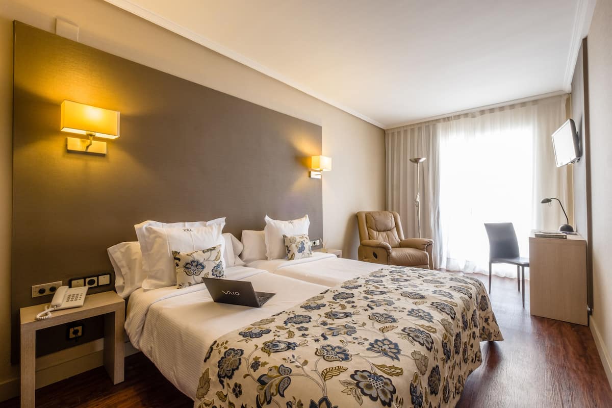 A hotel room with two beds, a desk, a chair, and a phone on a nightstand.