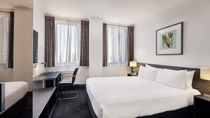 A hotel room with a bed, desk, chair, and a painting on the wall.