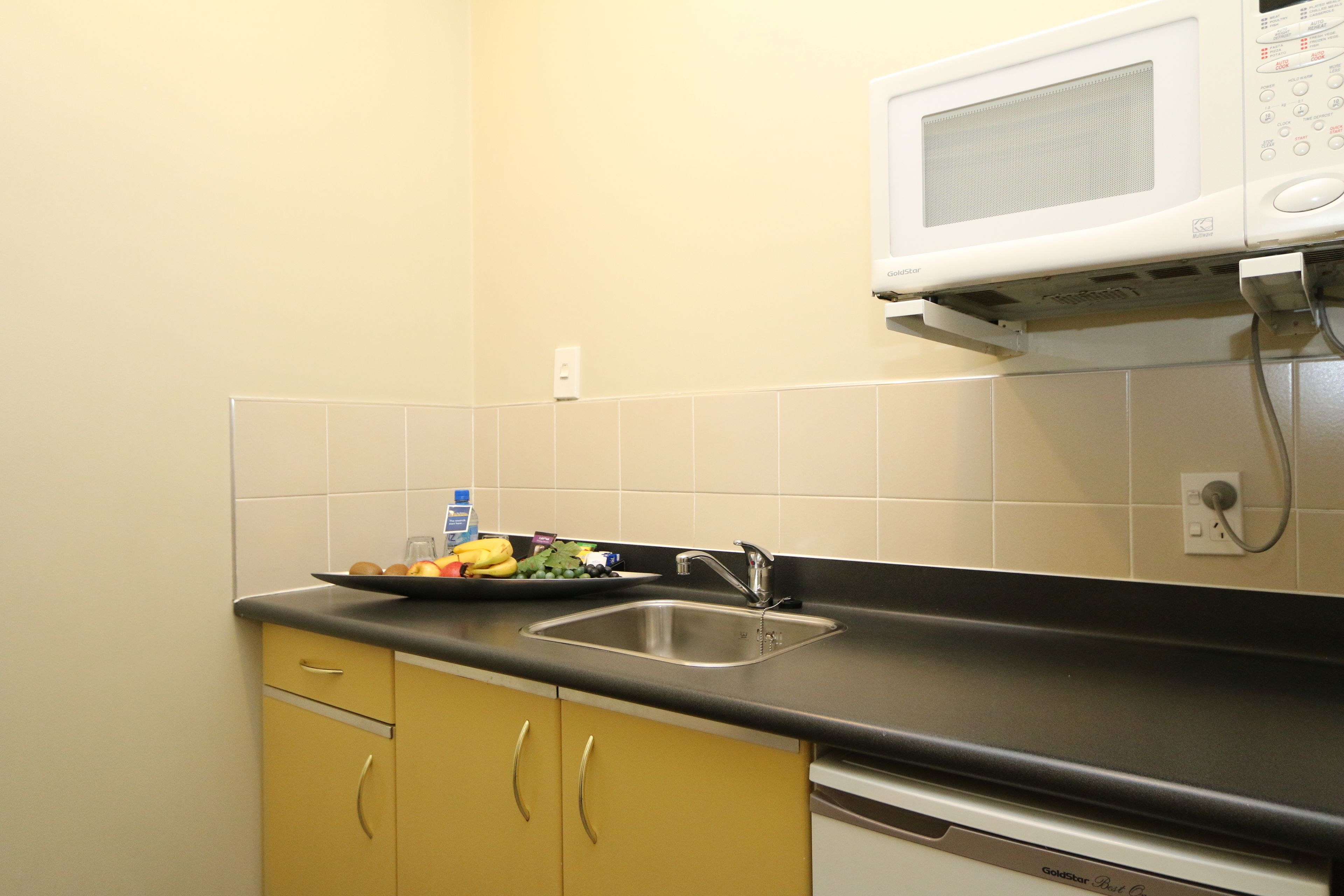 A kitchen with a sink, a microwave, and a dish rack with fruits and vegetables.