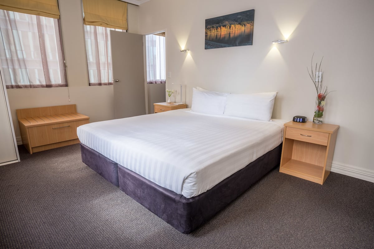 A neatly arranged hotel room with a large bed, bedside tables, a nightstand, a mirror, and a painting on the wall.