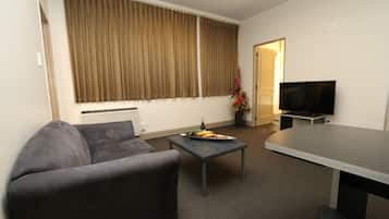 Een woonkamer met een bank, een bijzettafeltje met eten, een televisie en een deur naar een andere kamer.