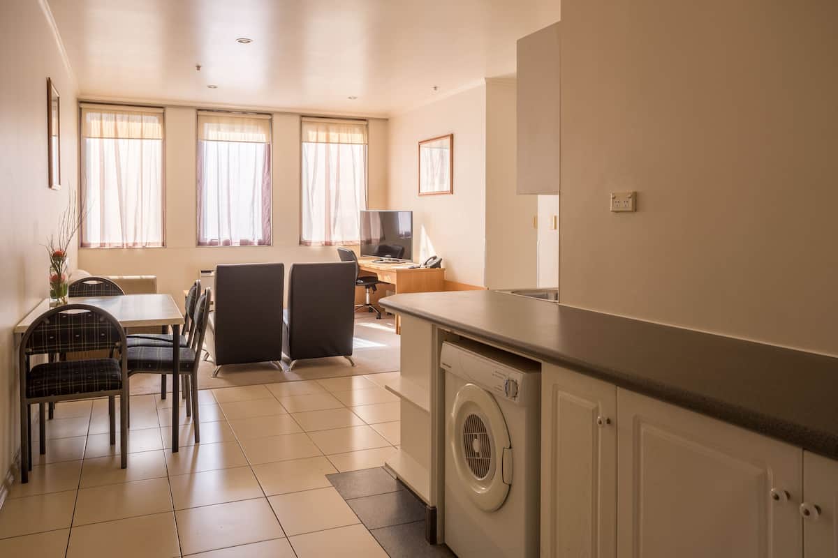 A compact hotel room with a dining area, a washing machine, and a desk with a computer.