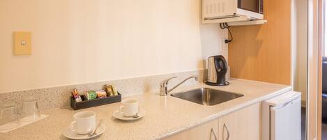 Una kitchenette con microondas, pileta y cafetera. Hay dos tazas en la encimera.