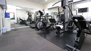 A gym with various exercise machines, a mirrored wall, and a tiled floor.