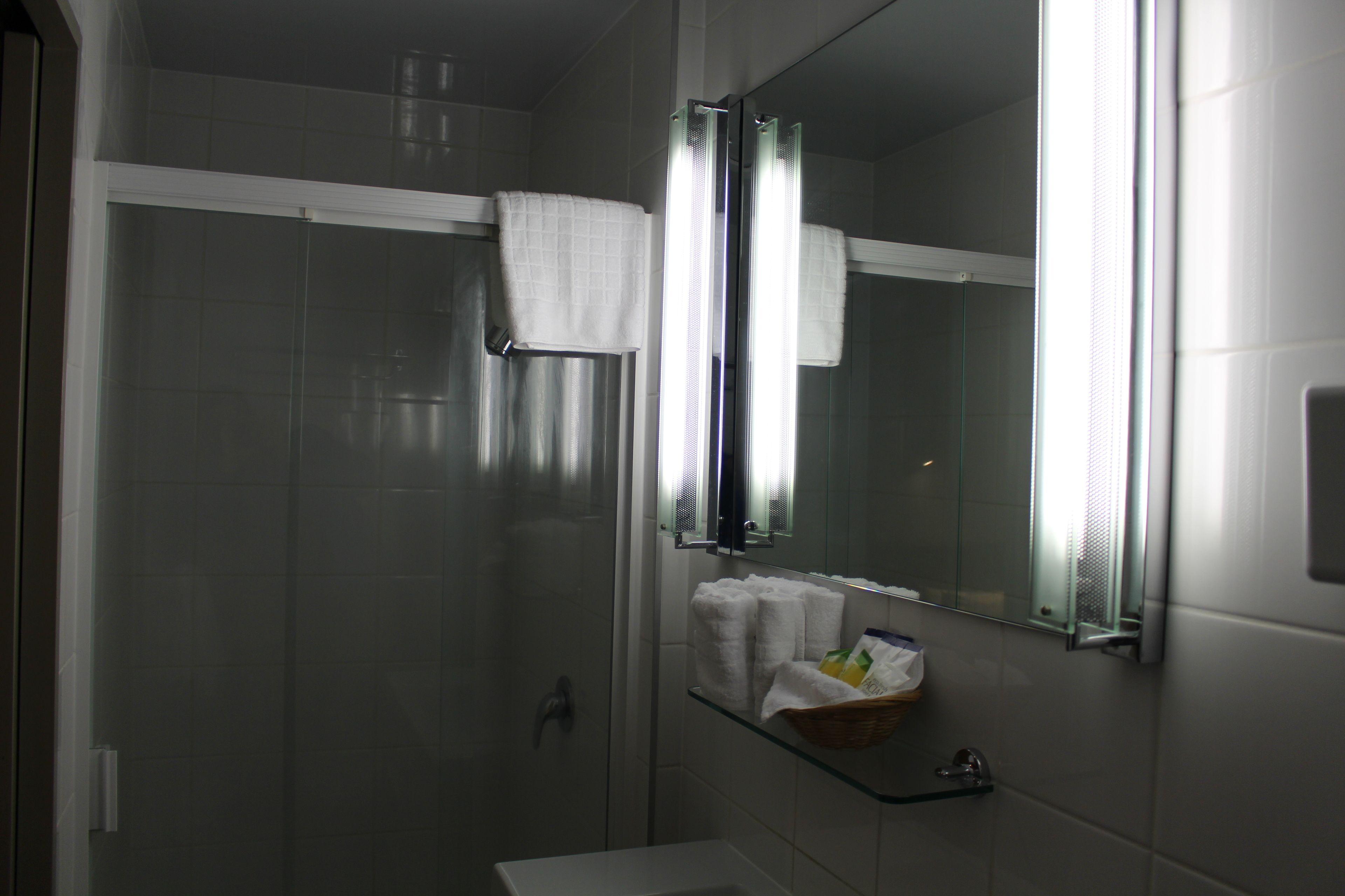A modern bathroom with a glass shower enclosure, a white sink, and a mirror with a towel rack.