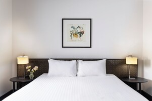 A hotel room with a neatly made bed, two bedside tables with lamps, and a framed botanical illustration on the wall.