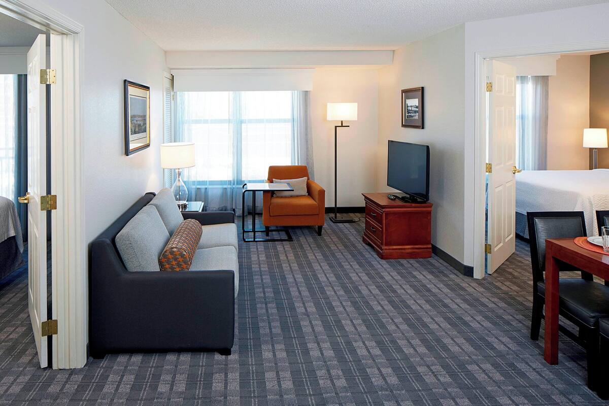 Ein Hotelzimmer mit Sofa, einem kleinen Tisch, Fernseher, Bett und Schreibtisch.