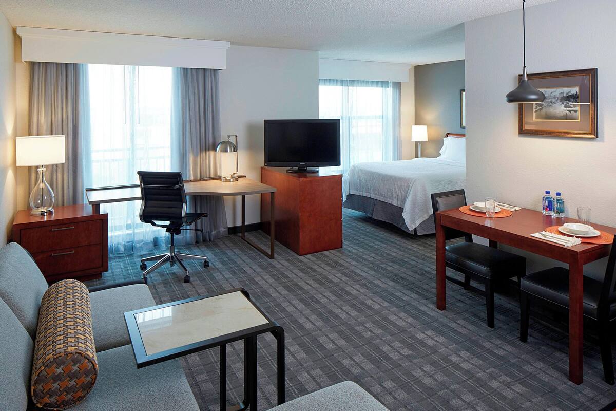 Ein Hotelzimmer mit Bett, Schreibtisch mit Fernseher, Sofa, kleinem Tisch und Essbereich mit Tisch und Stühlen.