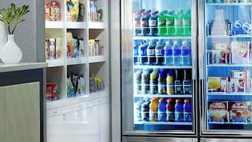 A vending machine area with snack and drink options, a refrigerated section with beverages, and a small plant on the counter.
