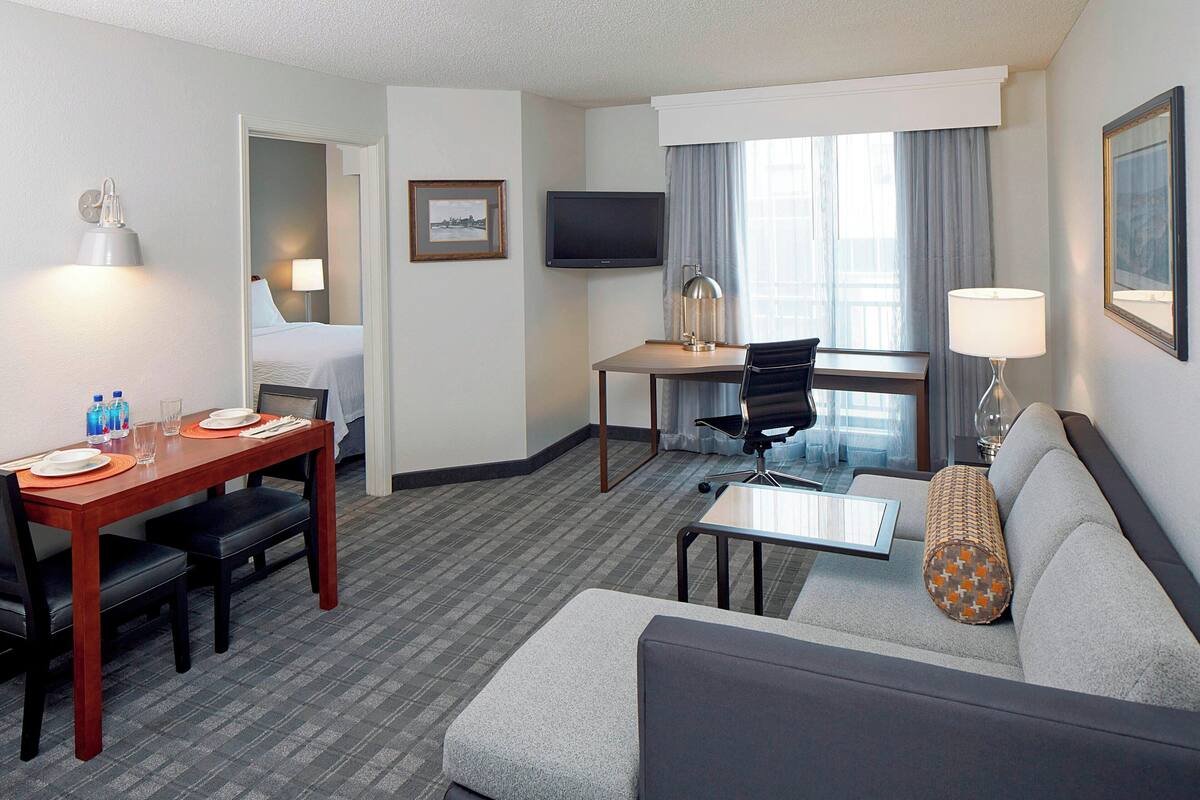 Ein Hotelzimmer mit Bett, Schreibtisch, Fernseher, Sofa und einem Essbereich mit Stühlen und Tisch.