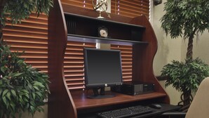 A wooden desk with a computer monitor, keyboard, and mouse. There is a clock above the monitor and a plant to the right. - Residence Inn by Marriott Oklahoma City South (Oklahoma City)