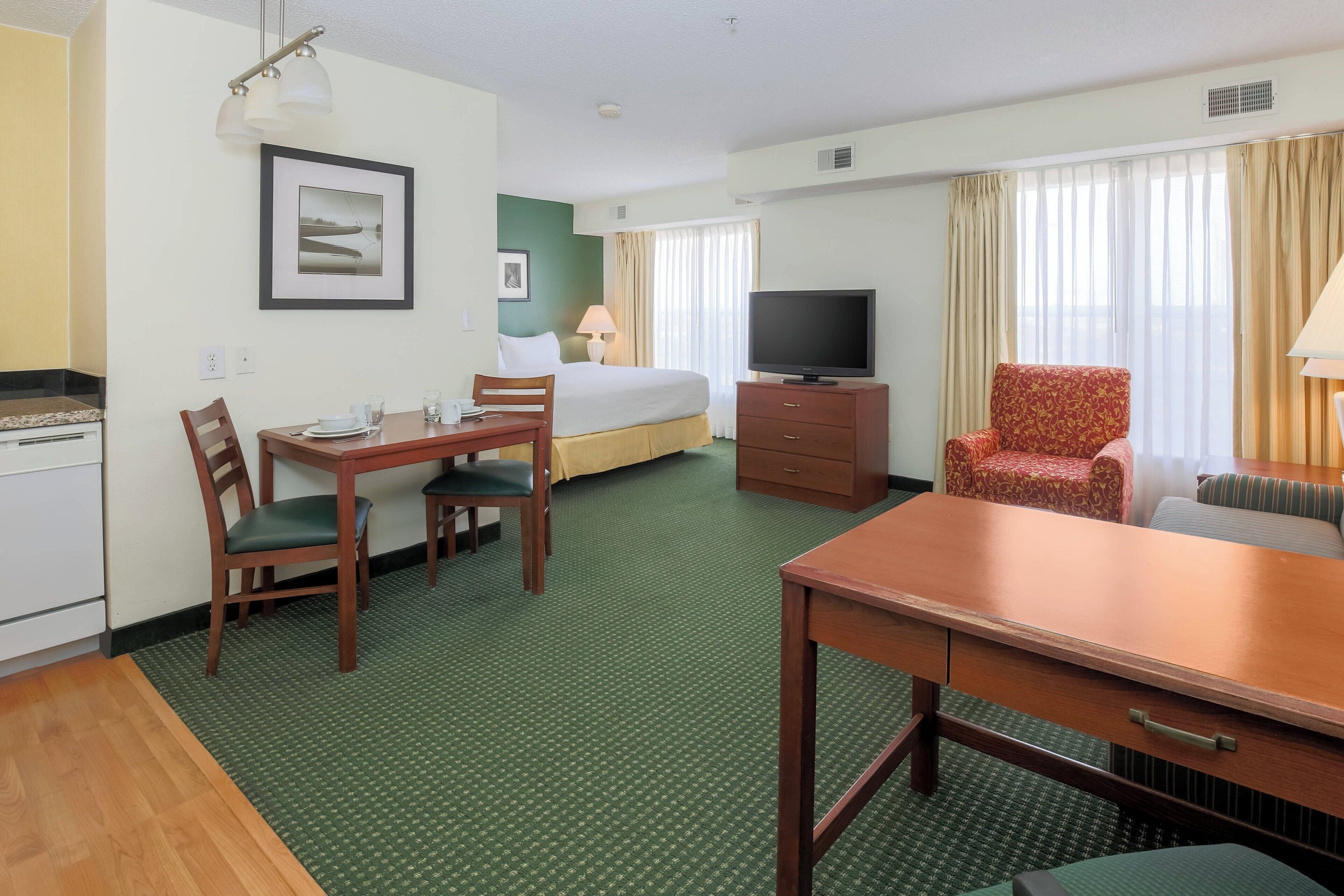 A hotel room with a bed, a TV, a dining table with chairs, a sofa, and a window with curtains.